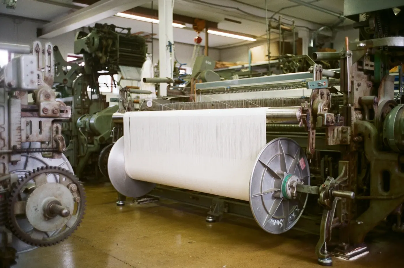 A weaving loom with a roll of white cloth on a factory floor
