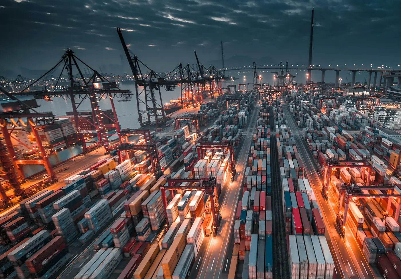 A container port at dusk, cranes over stacked export cargo